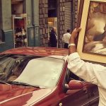 A image of a car with a red car in it and a shop and a man carrying a portrait