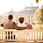 A couple sitting on a bench in a garden looking at a house