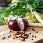 An onion cut up with veg in the background with peppercorns on a board